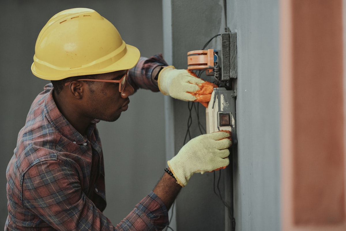 An electrician in a hard hat testing a meter on a wall
