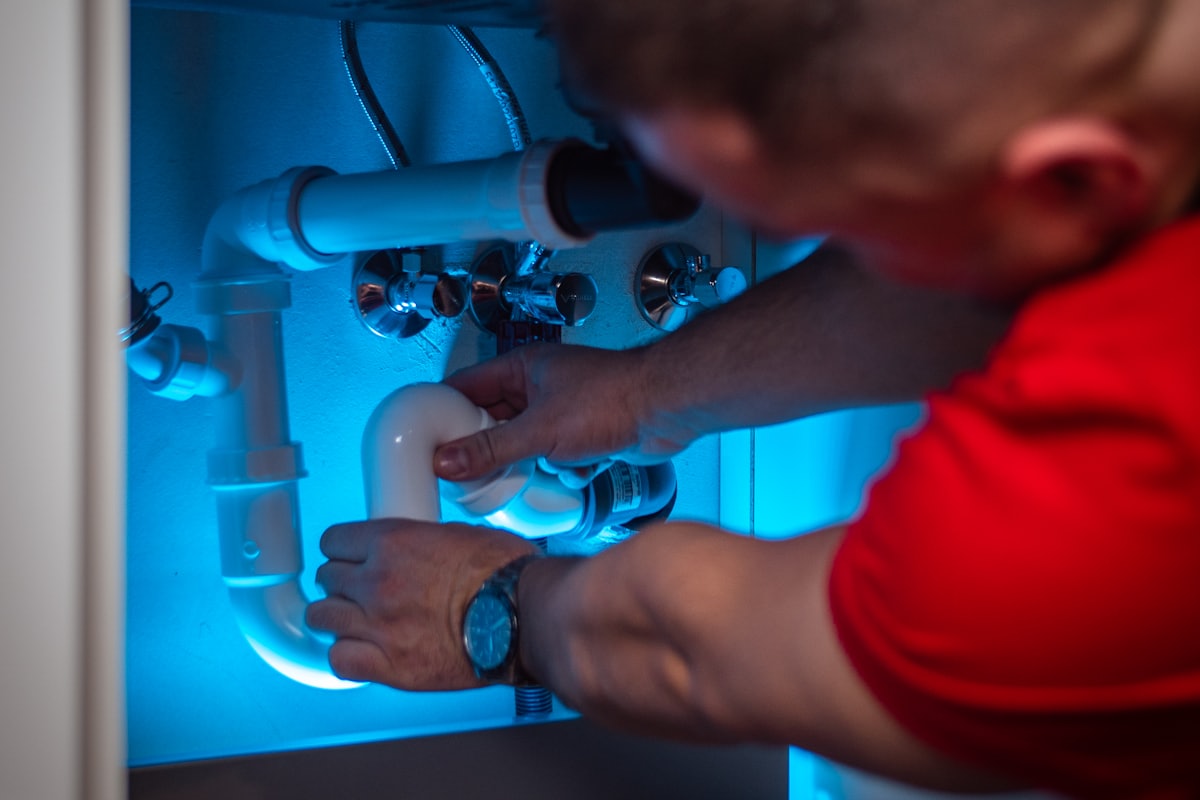 A plumber working under a sink with both hands on the pipework